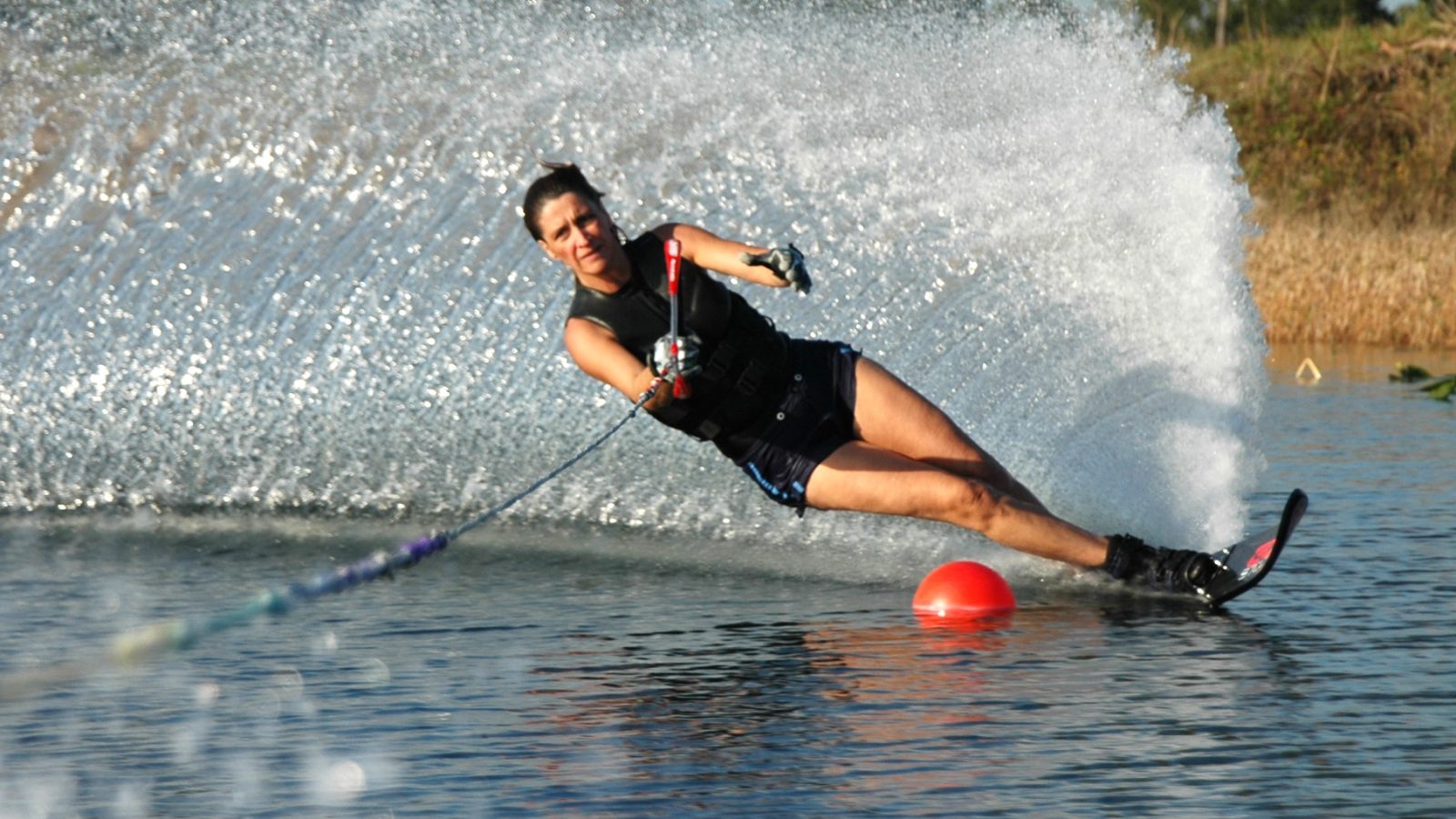 Skieur nautique en action, gerbe d'eau derriere lui, bouee rouge de slalom