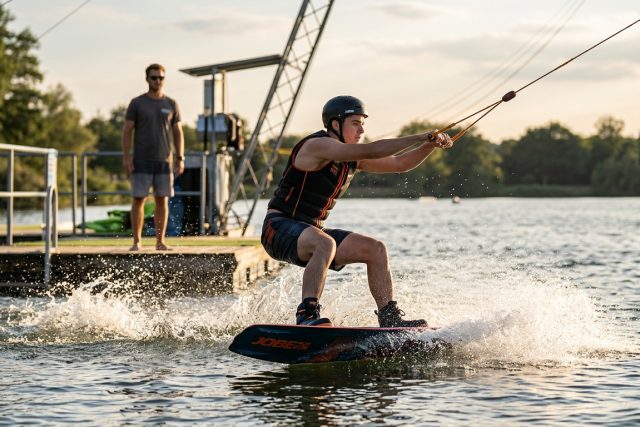 Rider débutant qui sort de l'eau au téléski nautique, genoux fléchis et bras tendus vers le palonnier